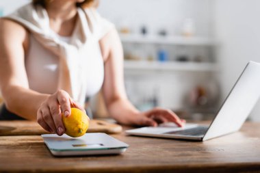Mutfak terazisine limon koyan ve dizüstü bilgisayar kullanan bir kadın. 