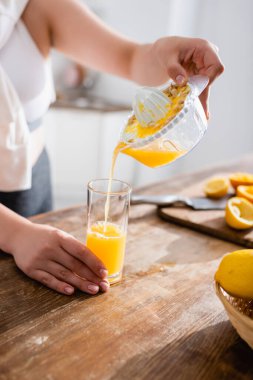 cropped view of woman pouring fresh orange juice in glass near squeezed fruits  clipart