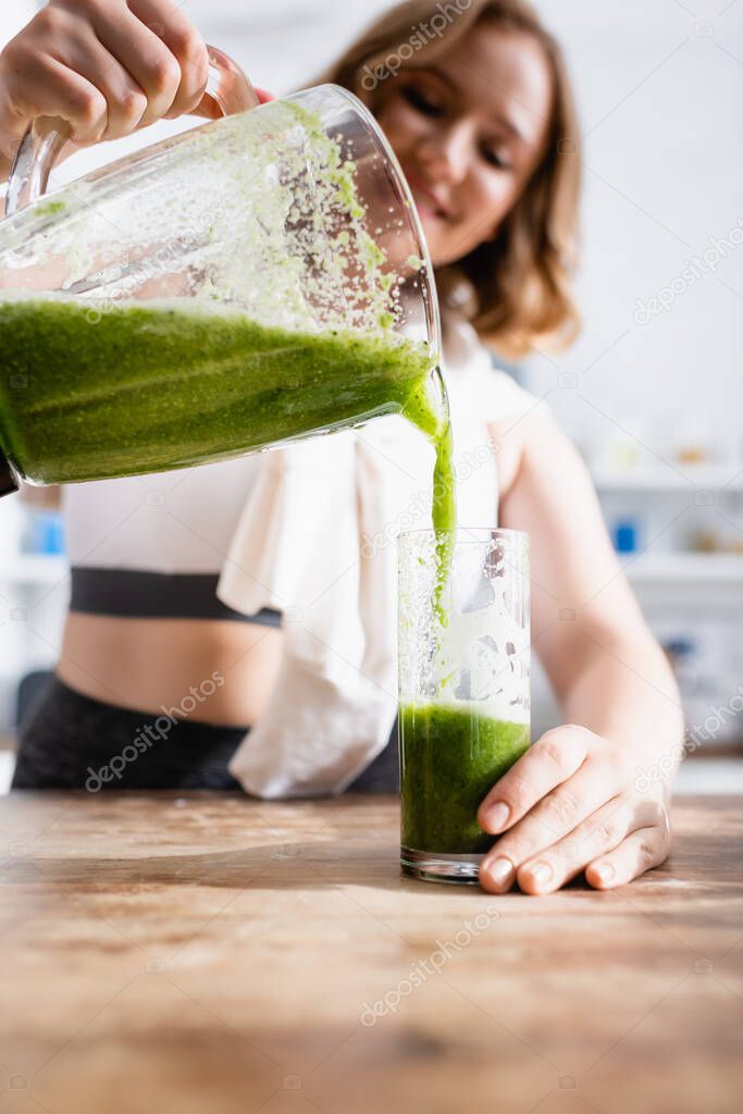 selective focus of woman pouring green smoothie in glass 