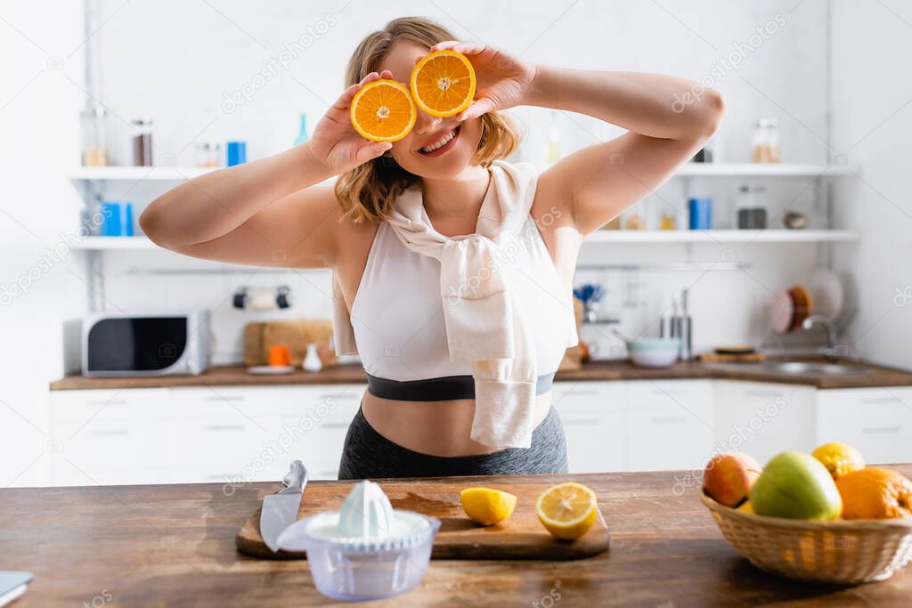 selective focus of woman covering eyes with halves of oranges 