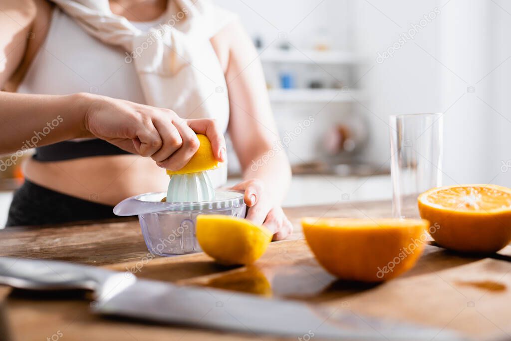 cropped view of woman holding half of orange near juicer while squeezing fruit  