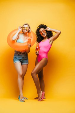 Kokteylli ve yüzme yüzmeli heyecanlı ırklar arası arkadaşlar sarı gözlüklü güneş gözlüğüne dokunuyor.