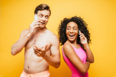 Afro-Amerikan mayo giymiş kadın ve sarı üzerinde akıllı telefonlardan konuşan üstsüz adam.