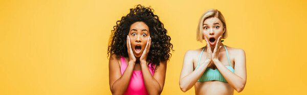 shocked interracial women in summer outfit touching faces isolated on yellow, horizonal image