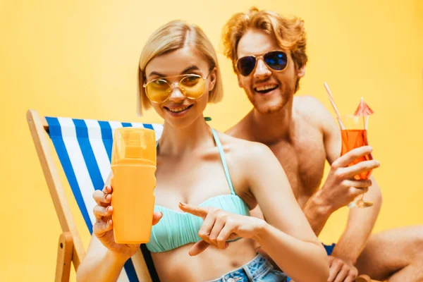 Sarışın kadın portakal suyunu işaret ediyor. Yanında sarı bardaklı bir adam var.