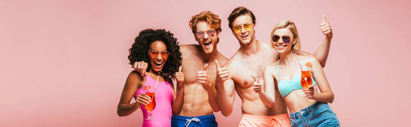 горизонтальное изображение взволнованных мультикультурных друзей, показывающих большие пальцы вверх, держа коктейльные бокалы, изолированные на розовом