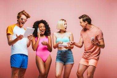 Heyecanlı Afro-Amerikalı kadın akıllı telefondan konuşurken çok kültürlü arkadaşları pembe renkte izole edilmiş aletler kullanıyor.