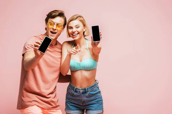 Young Friends Sunglasses Swimsuit Showing Smartphones Blank Screens Pointing Finger — Stock Photo, Image