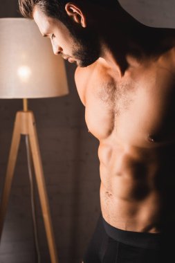 İç çamaşırlı, gömleksiz bir adam evine bakıyor. 