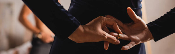 Панорамная концепция молодой женщины, снимающей обручальное кольцо сзади с мужчиной без рубашки на заднем плане дома 