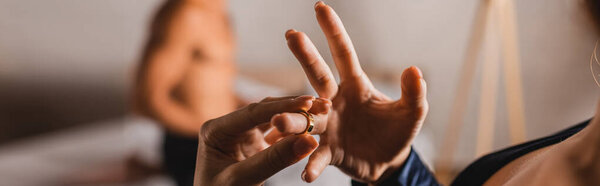 Horizontal crop of woman taking off golden ring with shirtless man at background in bedroom 