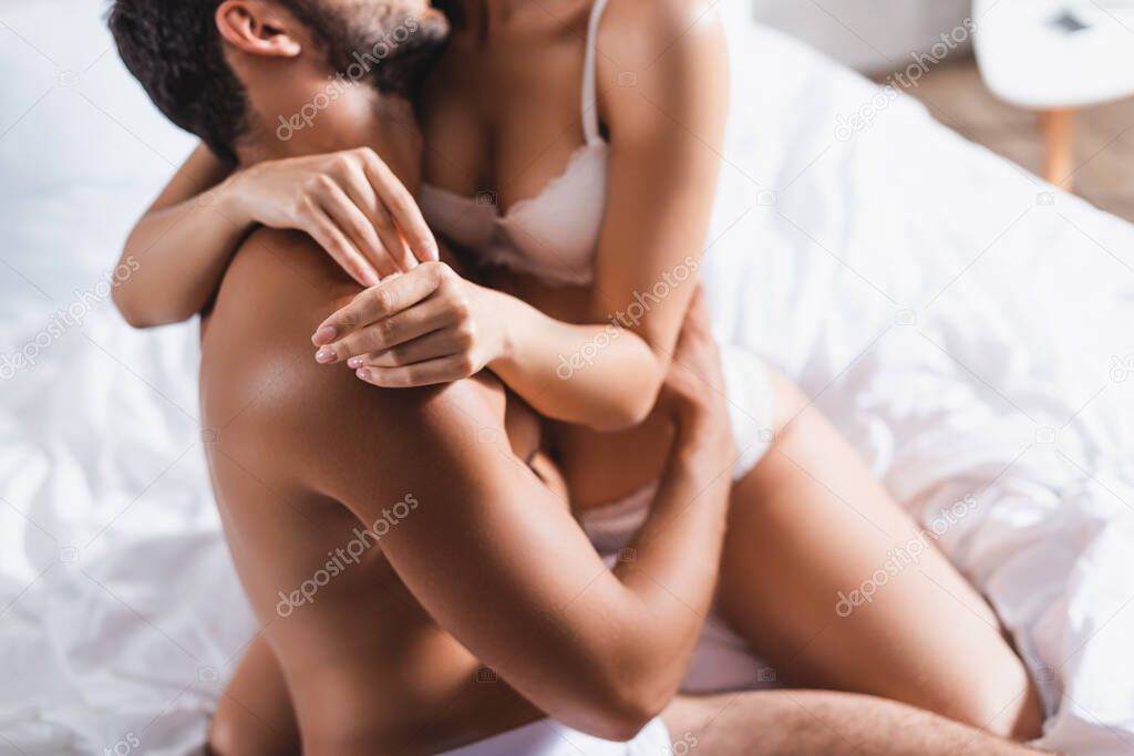 Cropped view of shirtless man hugging seductive woman on bed 