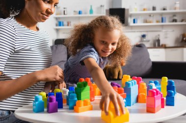 selective focus of african american girl taking building block while playing together with young nanny clipart