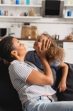 Çizgili tişörtlü genç Afrikalı Amerikalı anne mutfakta heyecanlı bir çocuğun kafasına dokunuyor.