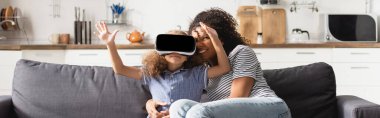 Genç Afro-Amerikan bebek bakıcısının video kulaklıklı kıza sarılırken çekilmiş panoramik bir fotoğrafı.