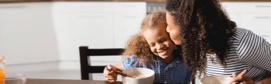 horizontal image of african american woman kissing daughter during breakfast  clipart