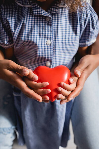 african american girl with mother holding heart model in cupped hands