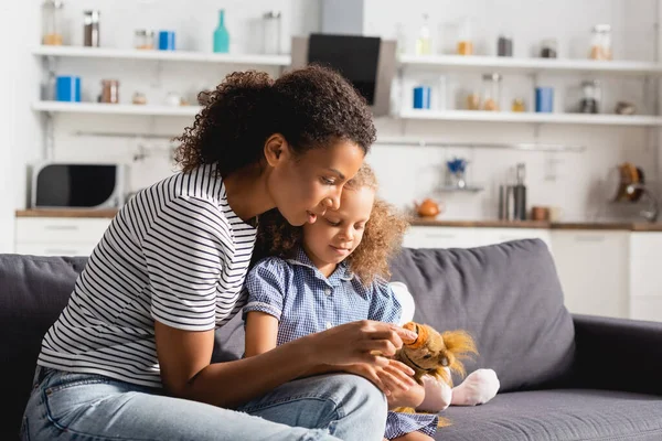 Young African American Babysitter Touching Toy Hands Girl Sitting Couch — Stock Photo, Image