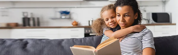 Imagem Horizontal Menina Americana Africana Abraçando Babá Sentado Sofá Livro — Fotografia de Stock