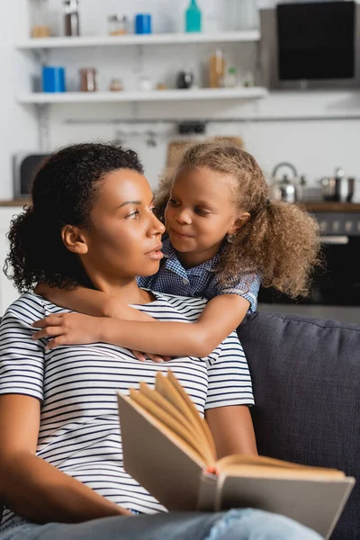 Enfoque Selectivo Niñera Afroamericana Sosteniendo Libro Mirando Chica Abrazándola Cocina —  Fotos de Stock