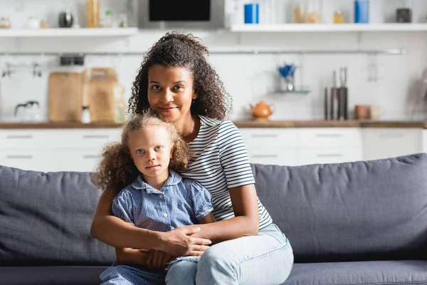 Joven Afroamericana Americana Mujer Abrazando Hija Mirando Cámara Mientras Sentado — Foto de Stock