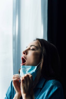 Tıbbi maskeli, ağzı açık, gözleri kapalı, korkmuş bir kadın. 