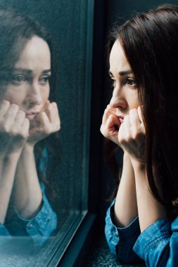 sad brunette woman touching face while looking at window  clipart