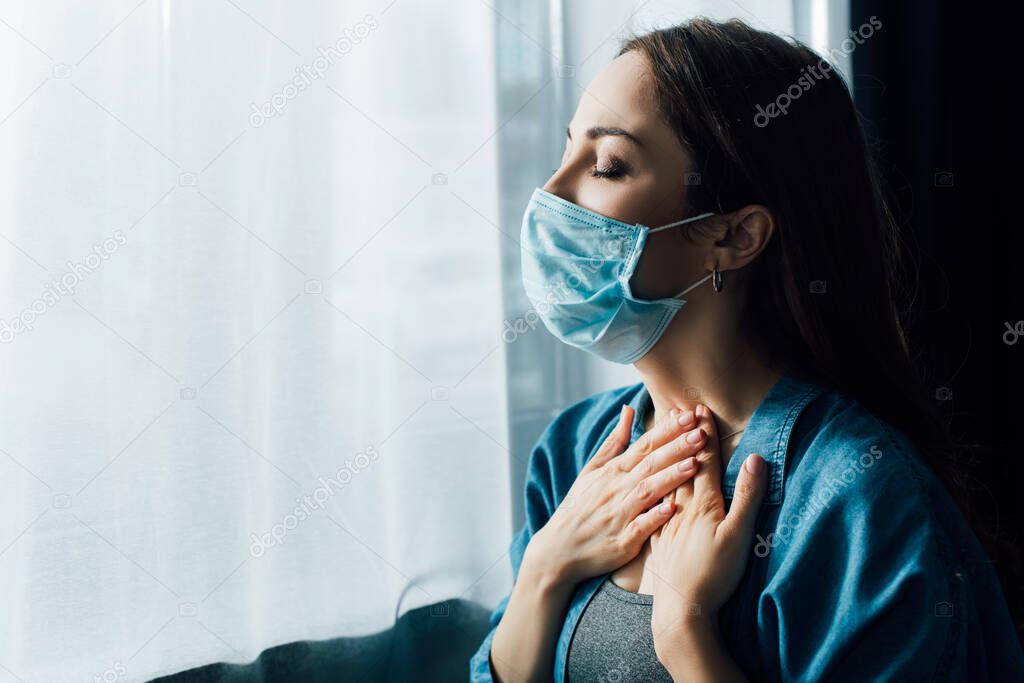 brunette woman in blue medical mask touching throat at home