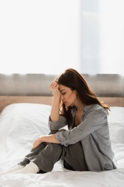 depresif esmer kadın gözleri kapalı yatakta oturuyor ve evde yüzüne dokunuyor.
