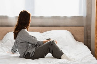 Yalnız esmer kadının arka manzarası evde yatakta oturuyor.