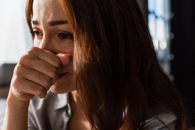 close up of upset and brunette woman touching face while crying at home clipart