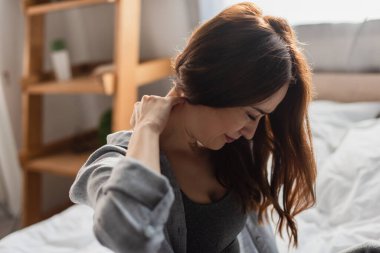 selective focus of upset brunette woman suffering from neck pain in bedroom clipart
