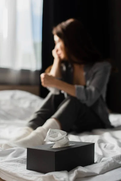 selective focus of tissue box on bedding near depressed woman