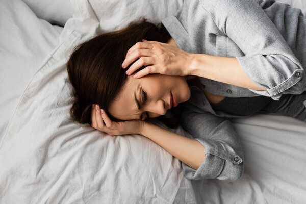 top view of tired woman having migraine, touching head and lying on bed