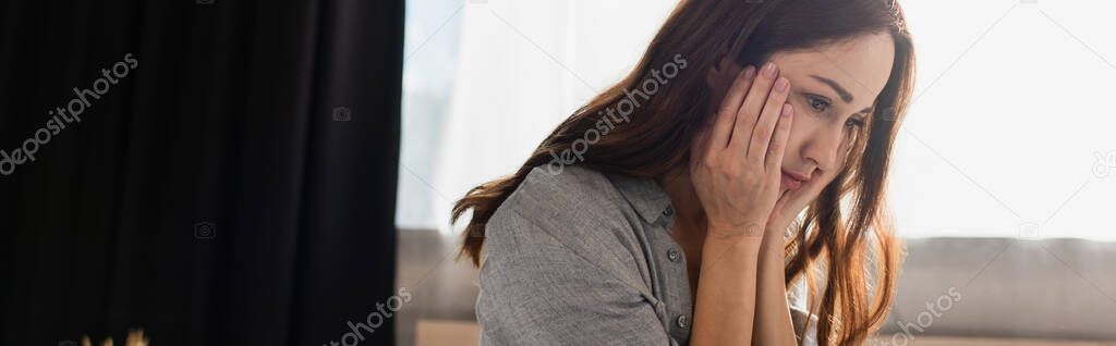 panoramic concept of depressed brunette woman touching face at home