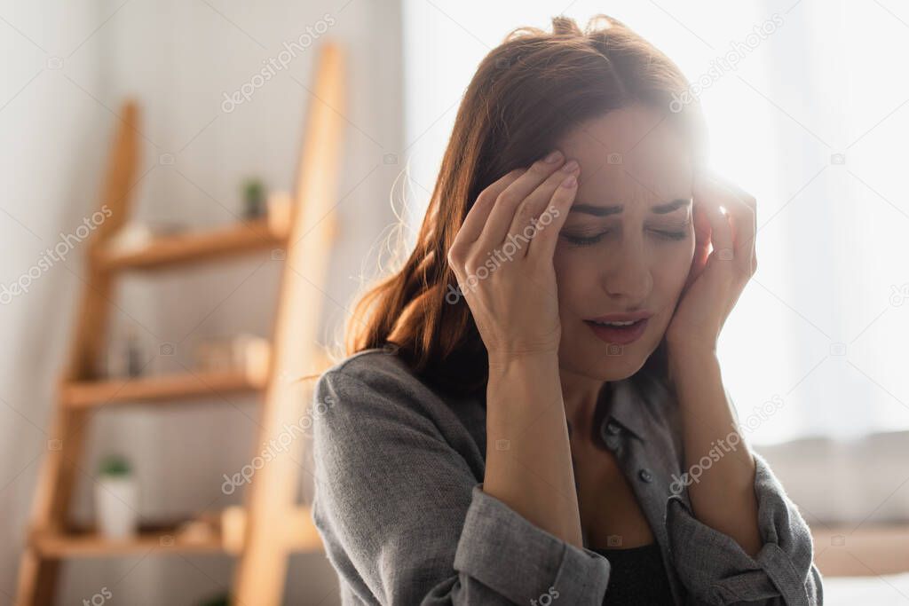 brunette woman with closed eyes suffering from pain and touching head at home