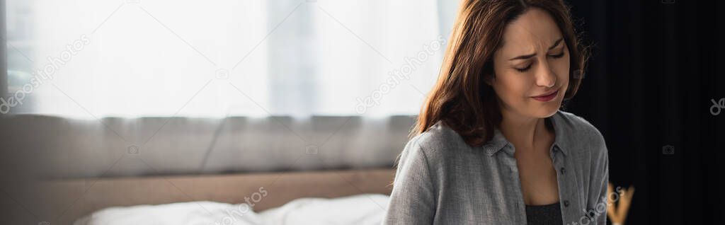 horizontal image of brunette woman with closed eyes suffering from pain in bedroom 