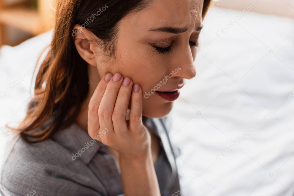 upset brunette woman with closed eyes touching face while suffering from toothache at home