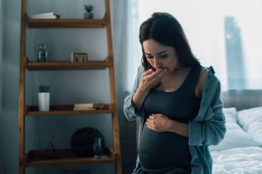 pregnant woman touching belly and covering mouth while having nausea at home clipart