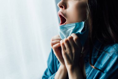 Tıbbi maskeye dokunan ağzı açık, korkmuş kadının kısmi görüntüsü 