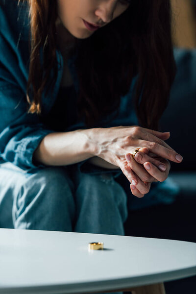 обрезанный вид брюнетки женщина сидит возле кофейного столика и снимая золотое кольцо, развод концепции 