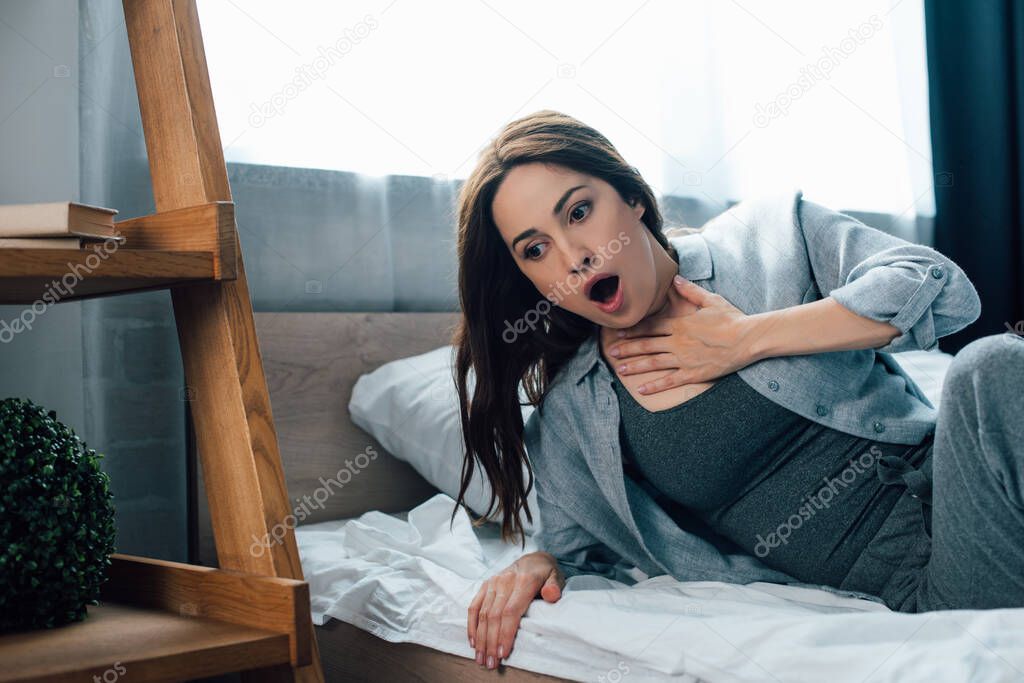 frightened brunette woman touching throat in bedroom 