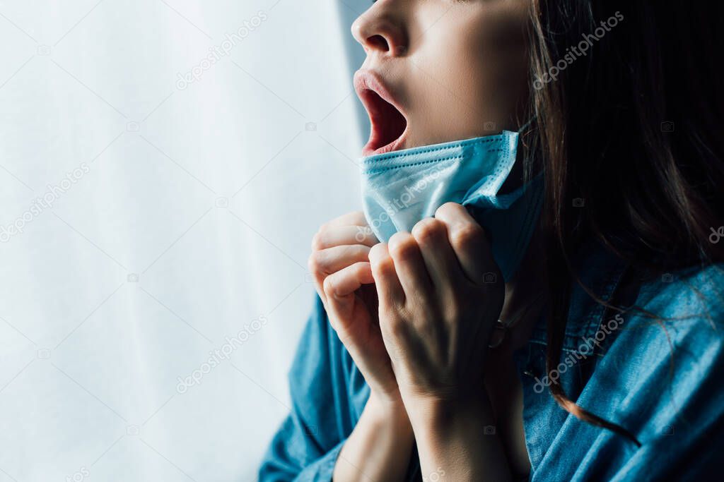 partial view of scared woman with open mouth touching medical mask 