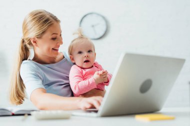 Annenin masada dizüstü bilgisayarla çalışırken bebeğe baktığı seçmeli bir odak noktası. 