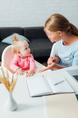 Seçici odak noktası, eliyle bebeği ve masadaki kırtasiyeyi gösteren kadın.
