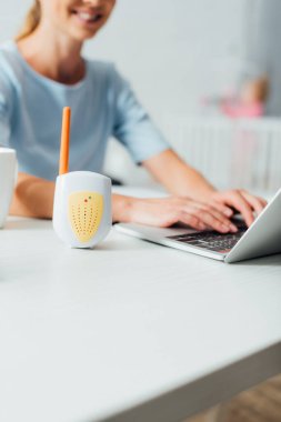 Selective focus of baby monitor near woman using laptop at table  clipart