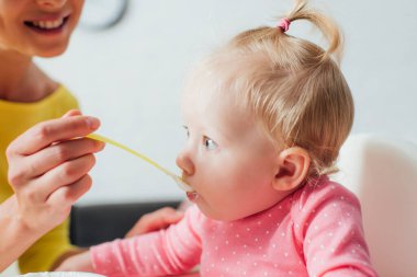 Selective focus of woman feeding daughter with baby food at home  clipart