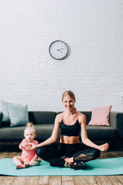 Woman in sportswear sitting in yoga pose near daughter on fitness mat 