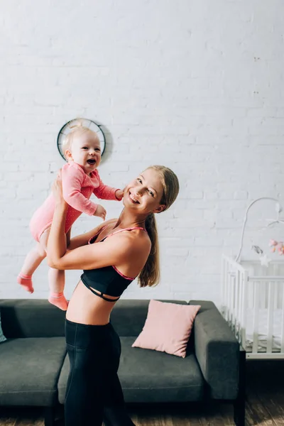 Mulher Sportswear Olhando Para Câmera Enquanto Segurando Filha Sala Estar — Fotografia de Stock