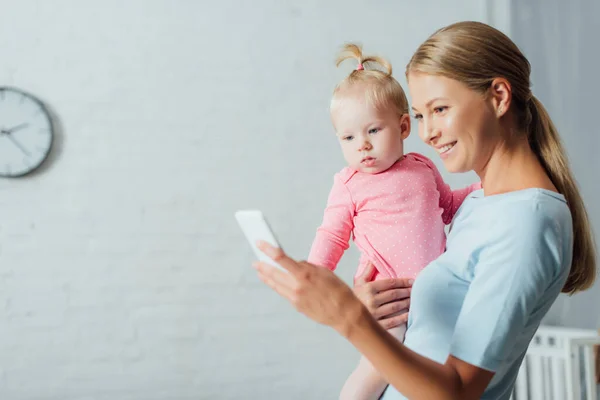 Foco Seletivo Mulher Usando Smartphone Enquanto Segura Filha Bebê Casa — Fotografia de Stock